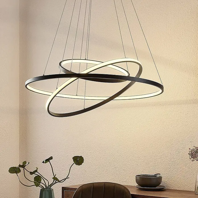 Lucande LED Pendelleuchte in schwarz matt, Hängelampe -  - Moderne LED-Pendelleuchte mit verschlungenen schwarzen Ringen, die warmweißes Licht abgeben, über einem Esstisch.