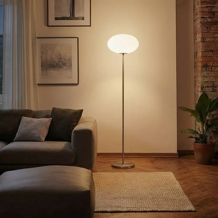 Lindby Stehlampe Wohnzimmer in nickel satiniert, weiß, Stehleuchte -  - Eine Stehleuchte mit kugelförmigem weißem Diffusor und dünnem, warmgetöntem Metallständer beleuchtet ein Wohnzimmer neben einem Sofa.