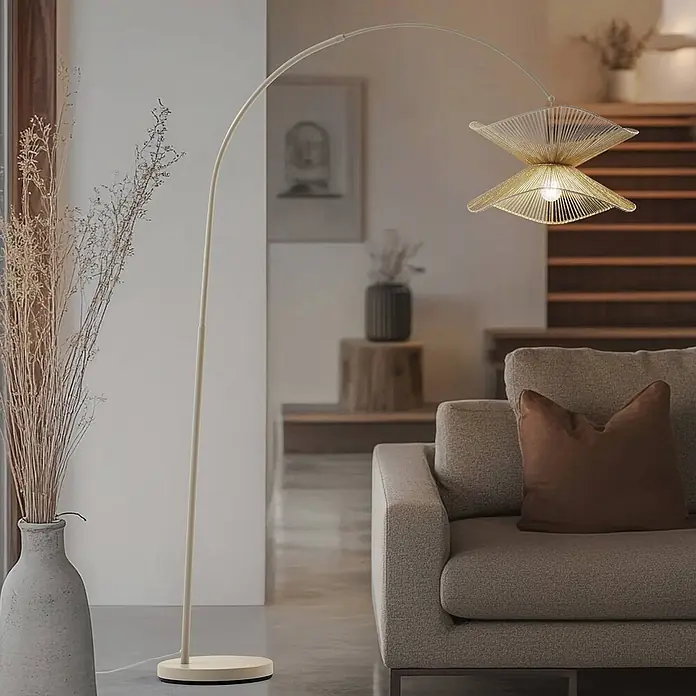 Lindby Stehleuchte Valdorin - creme / amber, creme / amber, E27 - Eine elegante Bogenstehleuchte mit goldenem geflochtenem Lampenschirm beleuchtet ein modernes Wohnzimmer neben einem Sofa.