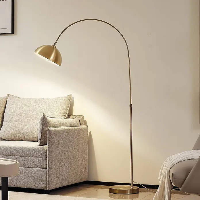 Lindby Stehlampe in messing, Bogenlampe Wohnzimmer -  - Goldene Bogenstehleuchte beleuchtet ein Wohnzimmer, neben einem hellen Sofa platziert.