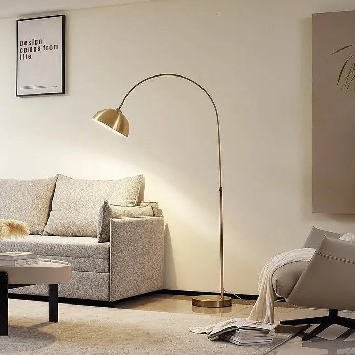 Lindby Stehlampe in messing, Bogenlampe Wohnzimmer -  - Eine moderne goldfarbene Bogenstehleuchte beleuchtet einen gemütlichen Wohnbereich, über einem hellen Sofa und Couchtisch platziert.