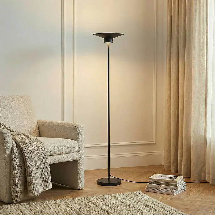 Lindby LED Stehlampe Wohnzimmer in schwarz, up down Stehleuchte -  - Schwarze Stehlampe aus Metall mit flachem, rundem Schirm, die ein Wohnzimmer neben einem cremefarbenen Sessel beleuchtet.
