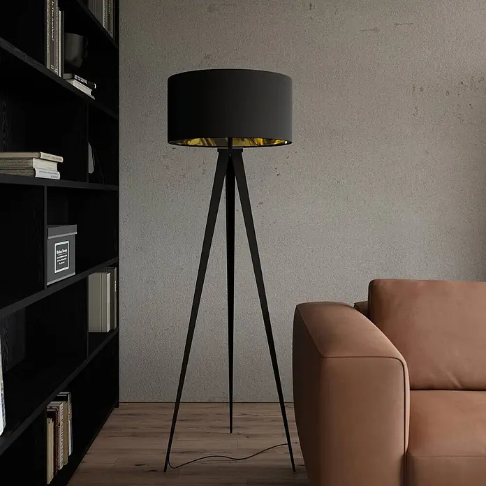Lindby Stehlampe Dreibein schwarz gold mit Fußschalter, ohne Leuchtmittel -  - Schwarze Tripod-Stehlampe mit goldener Innenseite, beleuchtet einen modernen Wohnraum.