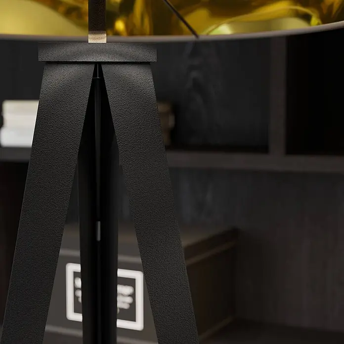 Lindby Stehlampe Dreibein schwarz gold mit Fußschalter, ohne Leuchtmittel -  - Nahaufnahme eines schwarzen, strukturierten Stativ-Lampenfußes mit goldenem Schirm in einem gedämpft beleuchteten Raum.