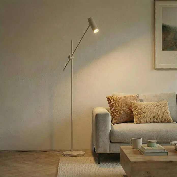 Lindby Stehlampe Wohnzimmer in beige, Stehleuchte -  - Moderne beige Stehleuchte aus Metall, die eine Wand im Wohnzimmer neben einem Sofa beleuchtet.
