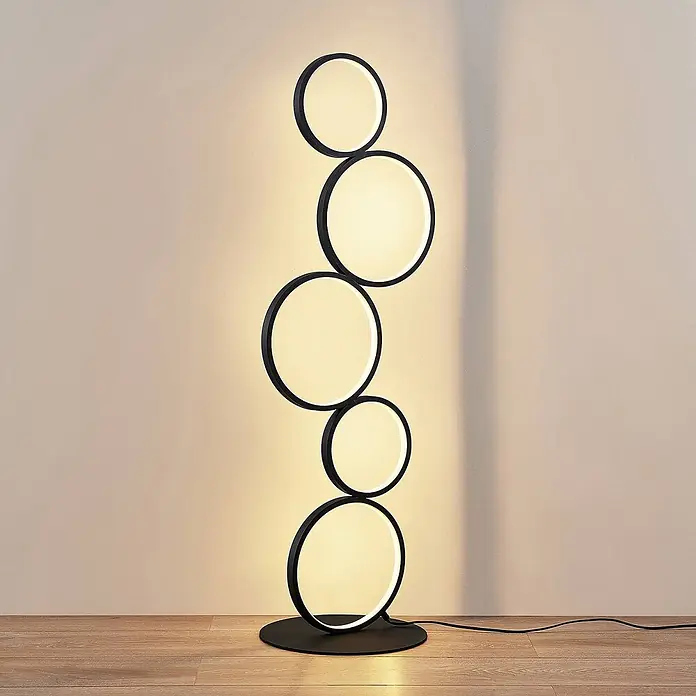 Lindby LED Stehlampe Wohnzimmer in schwarz, Stehleuchte -  - Moderne schwarze Stehleuchte mit fünf beleuchteten weißen Ringen, auf einem Holzfußboden stehend.