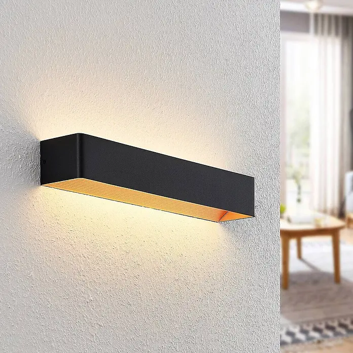 Arcchio LED Wandleuchte innen in schwarz, gold, Wandlampe -  - Schwarze, rechteckige Wandleuchte mit goldener Innenseite, spendet warmes Licht auf eine strukturierte Wand in einem modernen Raum.