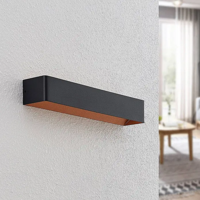 Arcchio LED Wandleuchte innen in schwarz, gold, Wandlampe -  - Schwarze, rechteckige Wandleuchte mit Kupfer-Innenseite an strukturierter Wand.