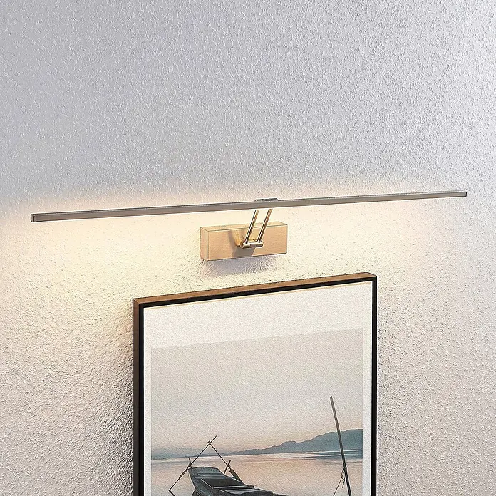 Lucande LED Bilderleuchte in nickel matt, Wandleuchte Bilderlampe -  - Bilderleuchte aus gebürstetem Metall mit Holzsockel, beleuchtet ein gerahmtes Kunstwerk an einer strukturierten Wand.