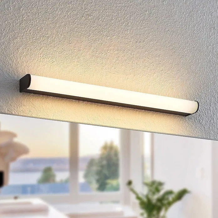 Lindby LED Wandleuchte innen in schwarz matt, weiß, Wandlampe -  - Schwarze lineare LED-Wandleuchte über einem Spiegel, leuchtet warmes Licht auf strukturierte Wand.
