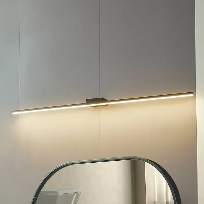 Lucande LED Wandleuchte innen in schwarz, Wandlampe -  - Moderne, schlanke, dunkelgraue LED-Spiegelleuchte über einem Spiegel, die warmes Licht abgibt.