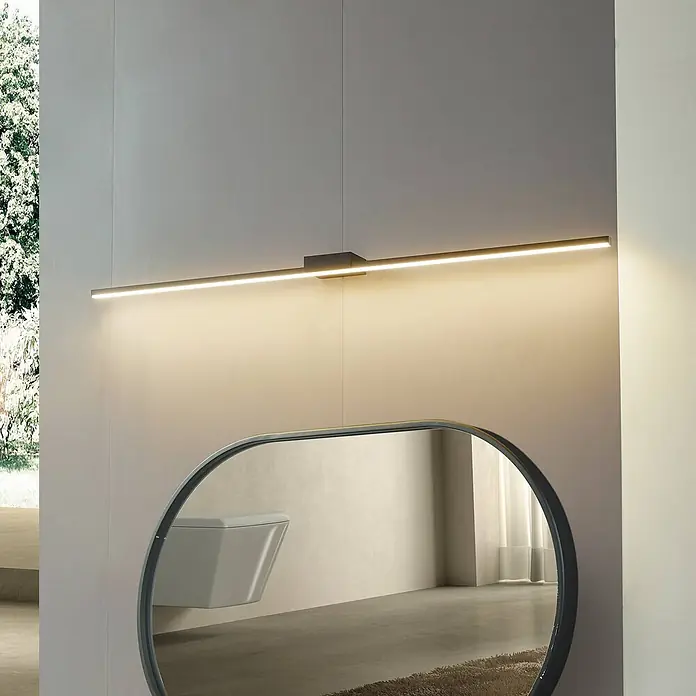 Lucande LED Wandleuchte innen in schwarz, Wandlampe -  - Lange, dunkle lineare LED-Wandleuchte über einem Spiegel, die warmes Licht in einem modernen Bad spendet.