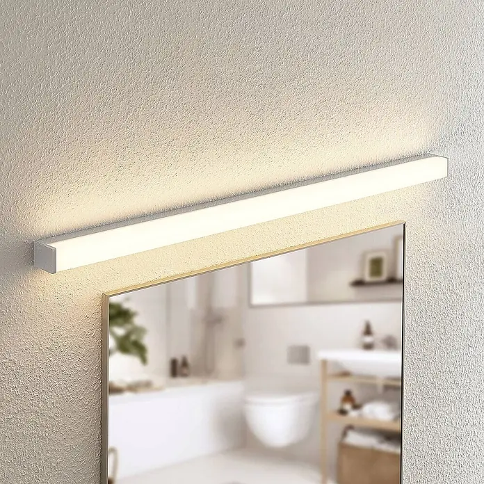 Lindby LED Wandleuchte innen in weiß, chrom, up down Wandlampe -  - Eine silberfarbene lineare LED-Spiegelleuchte mit weißem Diffusor, horizontal über einem Spiegel in einem modernen Badezimmer montiert.