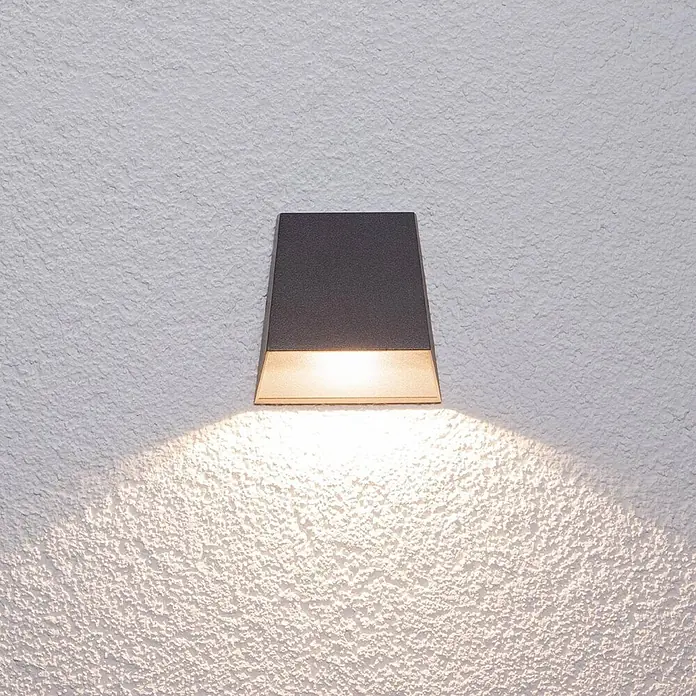 Lucande Außenwandleuchte Hanno - schwarz, schwarz, IP54 - Dunkelgraue, konische Wandleuchte wirft warmes Licht nach unten auf eine texturierte Wand.