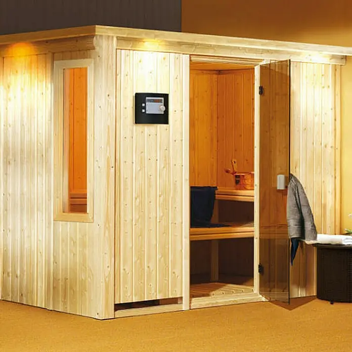 Karibu Elementsauna Gobin - Mit 9 kW Bio-Ofen mit externer Steuerung, Mit Dachkranz und Beleuchtung, L x B x H: 245 x 210 x 192 cm - Eine helle Holzsauna mit einer digitalen Steuerung und einer teilweise geöffneten Tür, die Einblick ins Innere bietet.