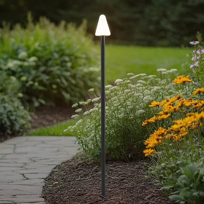 Lindby Erdspießleuchte Selinda -  - Schwarze Gartenwegleuchte mit weißem, konischem Kopf, neben einem Steinweg und Blumen platziert.