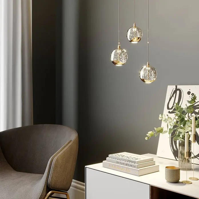 Lucande LED Pendelleuchte in transparent, gold, Hängelampe -  - Drei klare Glas-Pendelleuchten mit funkelndem Inneren und Goldakzenten, hängen in einem modernen Wohnraum.