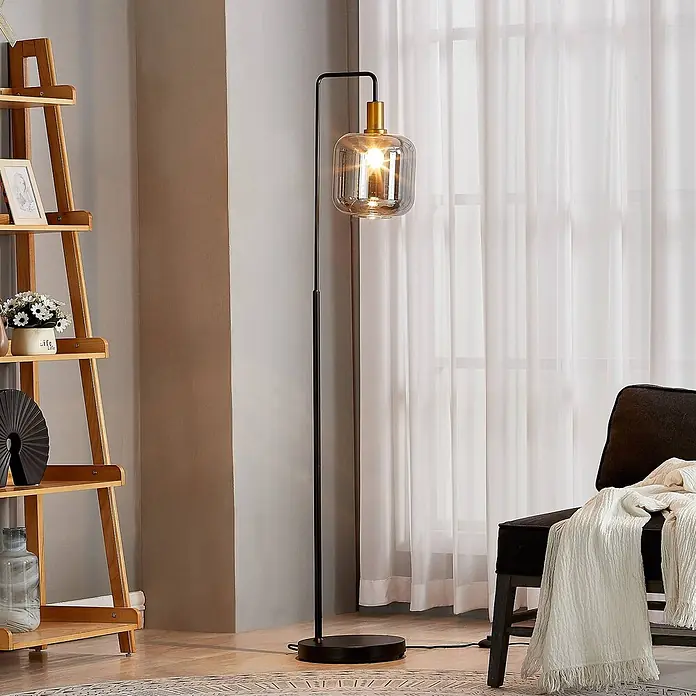 Lindby Stehlampe Wohnzimmer in gold, rauchgrau, Stehleuchte -  - Hohe Stehlampe mit schwarzem Metallsockel, Messingakzent und klarem geripptem Glasschirm, beleuchtet einen Raum.