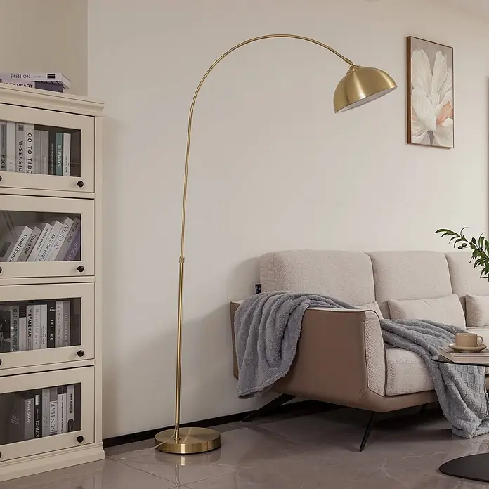 Lindby Stehlampe in messing matt, Bogenlampe Wohnzimmer -  - Goldene Bogen-Stehlampe mit kuppelförmigem Schirm, neben einem beigen Sofa in einem modernen Wohnzimmer.
