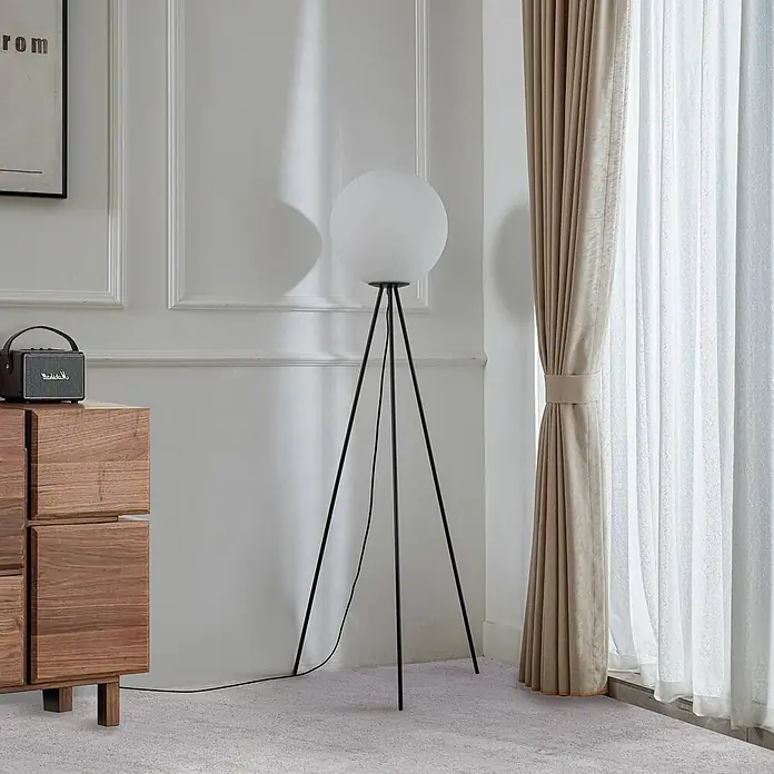 Lucande Stehleuchte Kestralia - schwarz, weiß / opal, E27 - Moderne Stehlampe mit weißem Kugeldiffusor und schwarzen Stativbeinen, in einem Raum neben einem Holzschrank und Vorhängen.