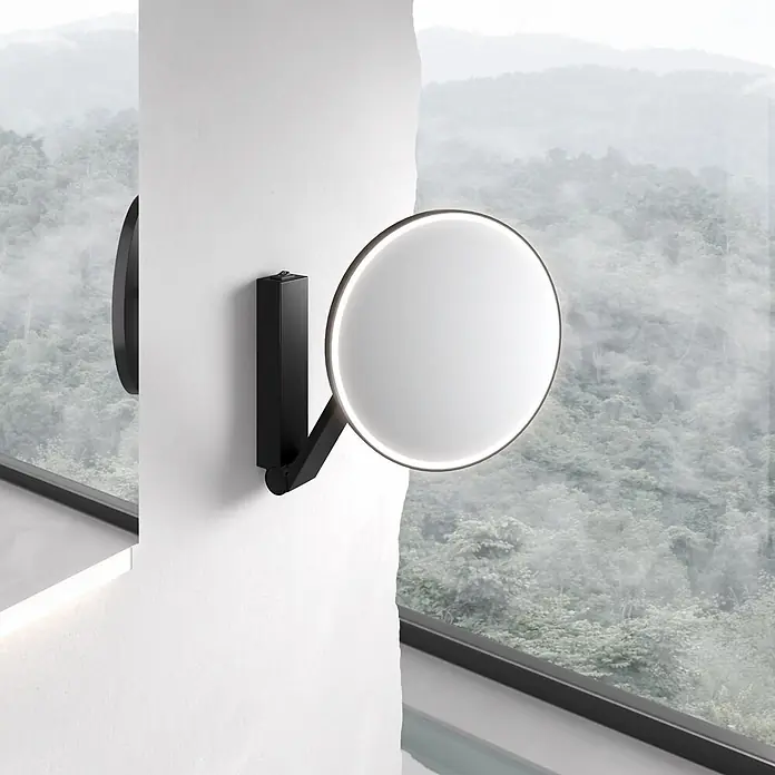 KEUCO iLook_move LED-Kosmetikspiegel rund Ø21,2 cm 5-fach schwarz matt -  - Schwarzer Wand-LED-Spiegel mit Ein-/Ausschalter an weißer Wand, mit Blick auf nebligen Wald.