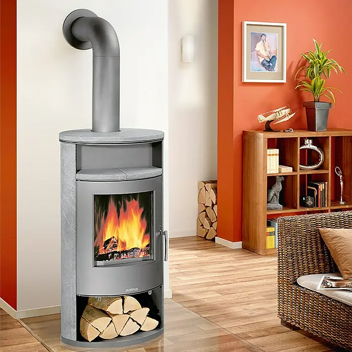 Justus Kaminofen Island Aqua - 10 kW, Raumheizvermögen: 200 m³, Material Verkleidung: Speckstein, Gussgrau - Bild eines Justus-Kaminofens im Wohnzimmer, der Wärme und Gemütlichkeit ausstrahlt. Der Ofen dient als stilvolle Heizquelle.