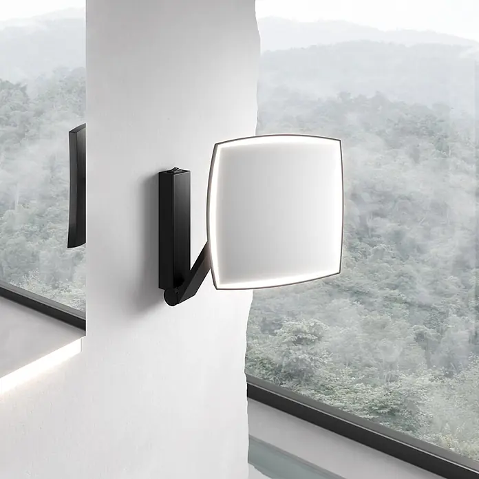 Keuco LED Kosmetikspiegel iLook move 20x20cm, mit Wippschalter, schwarz -  - Schwarze, verstellbare Wandleuchte mit leuchtendem, quadratischem Diffusor, an einer weißen Wand neben einem Fenster mit Blick auf einen nebligen Wald.