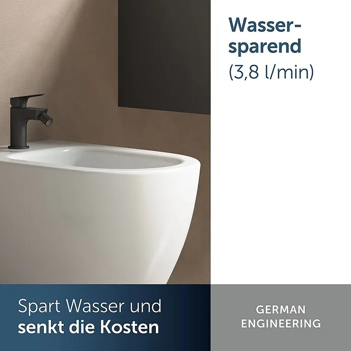 Ideal Standard Bidetarmatur Alero Schwarz Matt -  - Weißes Keramikbidet mit modernem, schwarzem Wassersparhahn vor einer warmgetönten Wand.