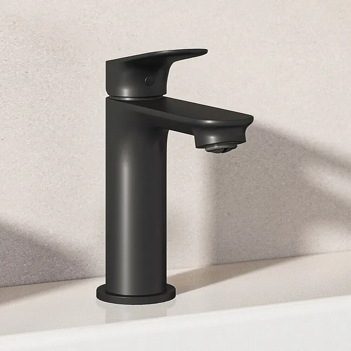 Ideal Standard Waschtischarmatur - Matt Schwarz, Matt - Moderner mattschwarzer Wasserhahn auf einem weißen Waschbecken vor einer hellen, strukturierten Wand.