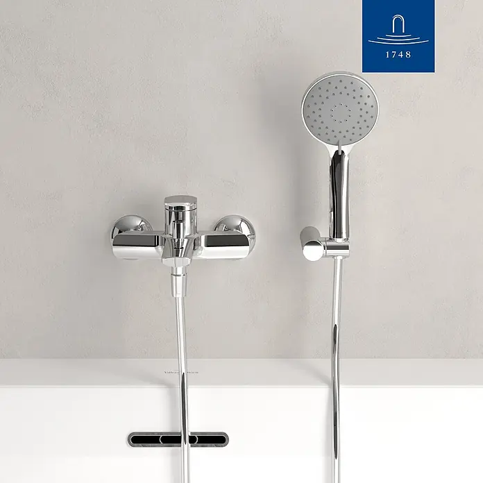 Villeroy & Boch Badewannenarmatur - Chrom, Hochglänzend - Verchromte Duscharmatur und Handbrause mit Schlauch, an der Wand über einem weißen Wannenrand montiert.