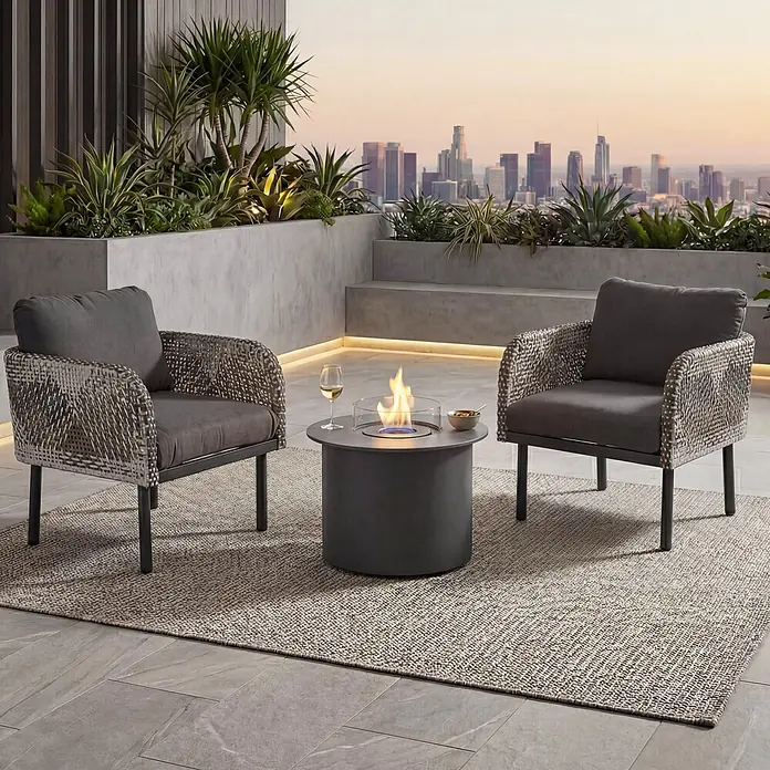 Mendler Loungemöbel-Set HWC-P80 - 3 -tlg., Rattan, Dunkelgrau, Dunkelgrau - Zwei geflochtene Outdoor-Loungesessel mit dunkelgrauen Kissen und ein runder dunkelgrauer Feuertisch auf einer Terrasse mit Stadtblick.