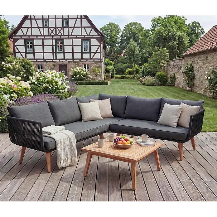 Mendler Loungemöbel-Set HWC-L30 - 3 -tlg., Holz, Polster dunkelgrau, Dunkelgrau - Graues Outdoor-Ecksofa mit schwarzen Flechtdetails und Holzbeinen, neben einem Holztisch auf einer Terrasse.