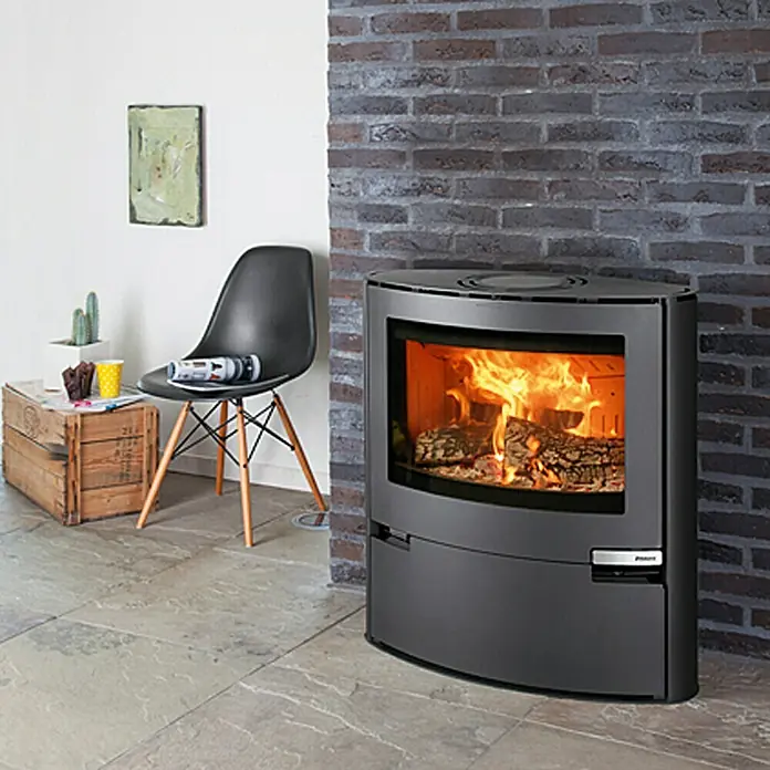 Aduro Kaminofen 15 - 6,5 kW, Raumheizvermögen: 350 m³, Material Verkleidung: Stahl, Schwarz - Ein moderner Kaminofen mit loderndem Feuer steht vor einer Backsteinwand und sorgt für eine gemütliche Atmosphäre im Raum.