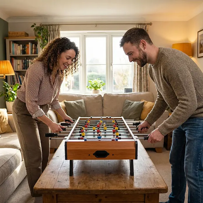 Homcom Tischkicker - L x B x H: 84,5 x 40 x 61,2 cm, Naturholz - Zwei Personen spielen an einem kompakten Kicker aus Holz mit schwarzen Griffen und farbigen Spielerfiguren.