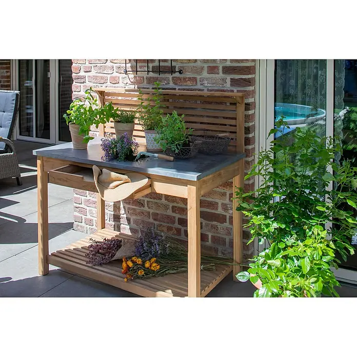 Bene Living Pflanzhilfe Hampton -  - Ein hölzerner Pflanztisch mit grauer Metallplatte, mit Pflanzen, Gartengeräten und einem Hut auf einer Terrasse.