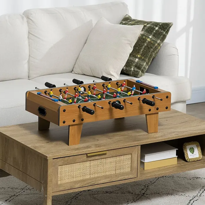 Homcom Tischkicker - L x B x H: 69 x 36,5 x 22 cm, Naturholz - Ein hölzerner Tischfußballtisch mit bunten Spielern und schwarzen Griffen, der auf einem hellbraunen Couchtisch im Wohnzimmer steht.