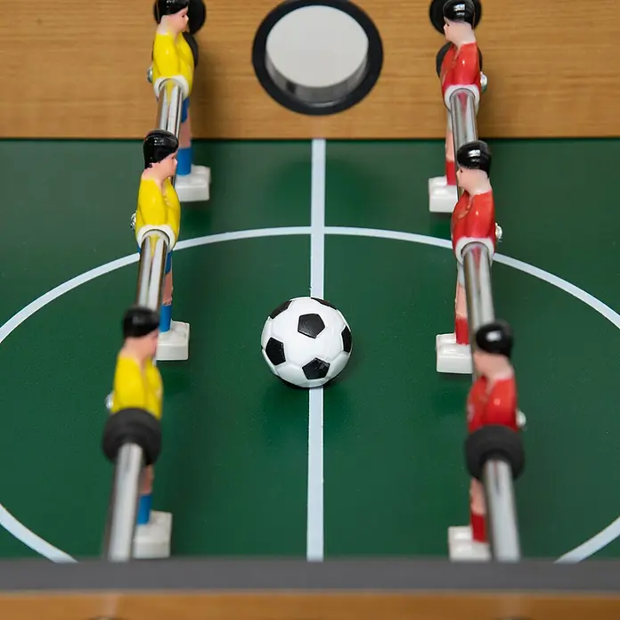 Homcom Tischkicker - L x B x H: 69 x 36,5 x 22 cm, Naturholz - Nahaufnahme eines Kicker-Tisches mit roten und gelben Spielern auf grünem Feld, zentriert auf einem schwarz-weißen Ball.