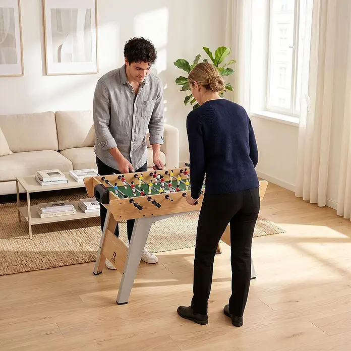 Sportnow Tischkicker - L x B x H: 121 x 87 x 77 cm, Naturholz - Zwei Personen spielen an einem hellen Holzkicker mit roten und gelben Spielern.