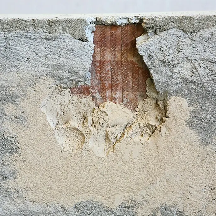Profi Depot Schnellreparatur-Mörtel - 25 kg - Beschädigte Betonwand mit freiliegenden Ziegeln und Putzresten.