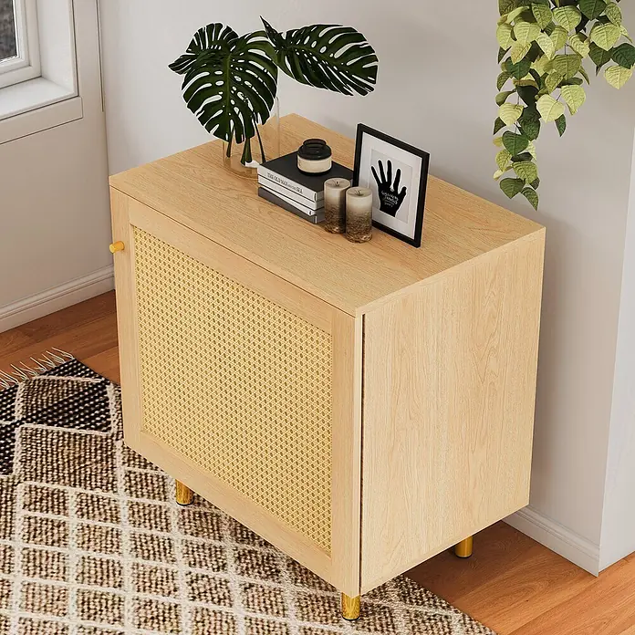 SONNENH Kommode - Natur - Heller Holzschrank mit Rattantür und goldenen Beinen, dekoriert mit Pflanzen, Büchern und Kerzen in einem Wohnraum.