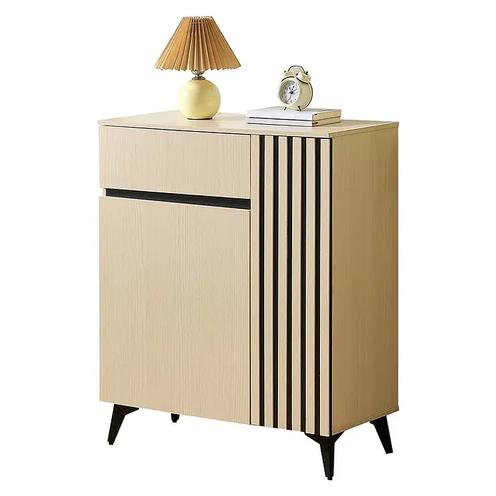 SONNENH Schuhschrank - Helle Holzoptik/Schwarz - Heller Holzschrank mit Schublade, Tür, schwarzen Lamellen und schrägen Beinen. Obenauf sind eine gelbe Lampe, Wecker und Bücher.