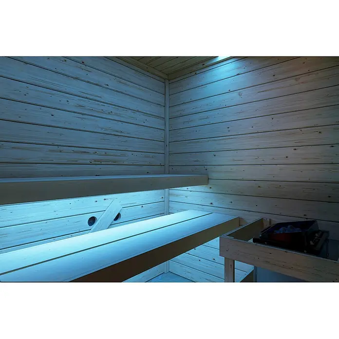 Karibu Elementsauna Oda Eck - Mit Ofen, L x B x H: 145 x 148 x 190,5 cm - Hölzernes Sauna-Interieur mit zweistufigen Bänken, blau beleuchtet. Ein Saunaofen mit Steinen ist sichtbar.