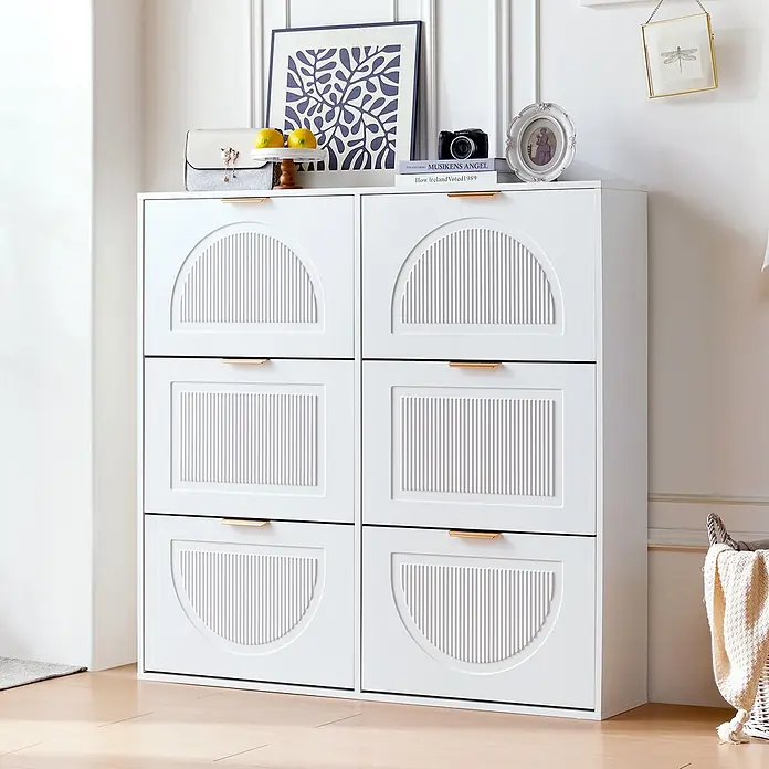SONNENH Schuhschrank mit 6 Klappen und Bogenfront, Weiß -  - Weißer Schrank mit sechs Kipptüren, gerilltem Design und goldfarbenen Griffen, in einem Raum mit Dekoration oben.