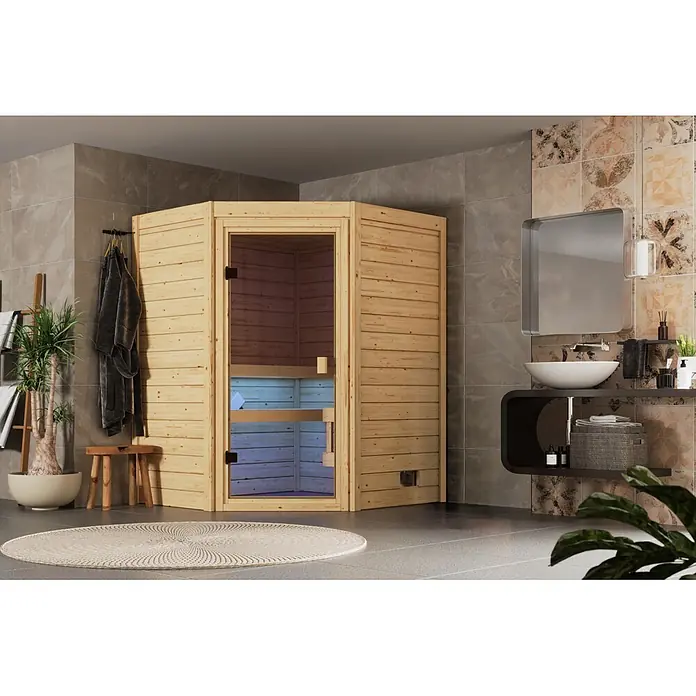 Karibu Elementsauna Oda Eck - Mit Ofen, L x B x H: 145 x 148 x 190,5 cm - Helle Ecksauna aus Holz mit Glastür, integriert in ein modernes Badezimmer mit Fliesenwänden und Waschtisch.