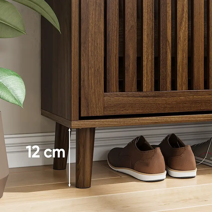 SONNENH Schuhschrank - Walnussoptik - Dunkelbrauner Holzschrank mit 12 cm hohen Beinen, darunter Schuhe. Eine grüne Pflanze steht daneben.