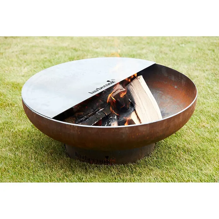 Barbecook Grillplatte Plancha - L x B: 75 x 32,5 cm, Kohlenstoffstahl - Barbecook Feuerschale aus Cortenstahl mit runder Schale und teilweise abgedeckter Kochplatte, mit brennenden Holzscheiten darin.