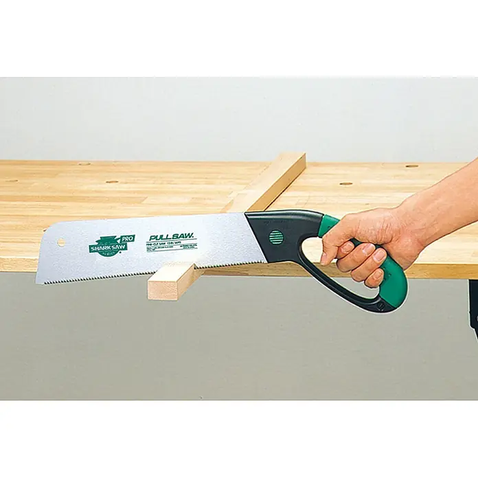 Famex Japansäge - Länge: 300 mm, Stahl - Grüne und schwarze Japansäge schneidet ein helles Holzstück auf einer Werkbank, von einer Hand gehalten.