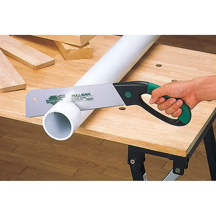 Famex Japansäge - Länge: 300 mm, Stahl - Person schneidet weißes PVC-Rohr mit einer grüngriffigen Zugsäge auf einer Holzwerkbank.