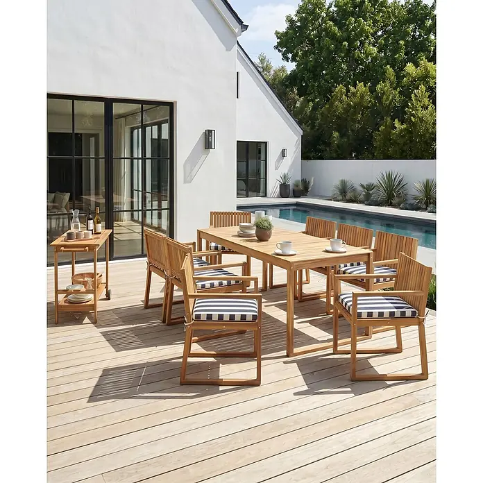 Beliani Gartenstuhl-Set SASSARI II - 8 Stk., zertifiziertes Akazienholz, Braun, B x T x H: 54 x 59 x 80 cm - Gartensitzgruppe und Servierwagen aus hellem Holz mit blau-weiß gestreiften Kissen auf einer Holzterrasse.