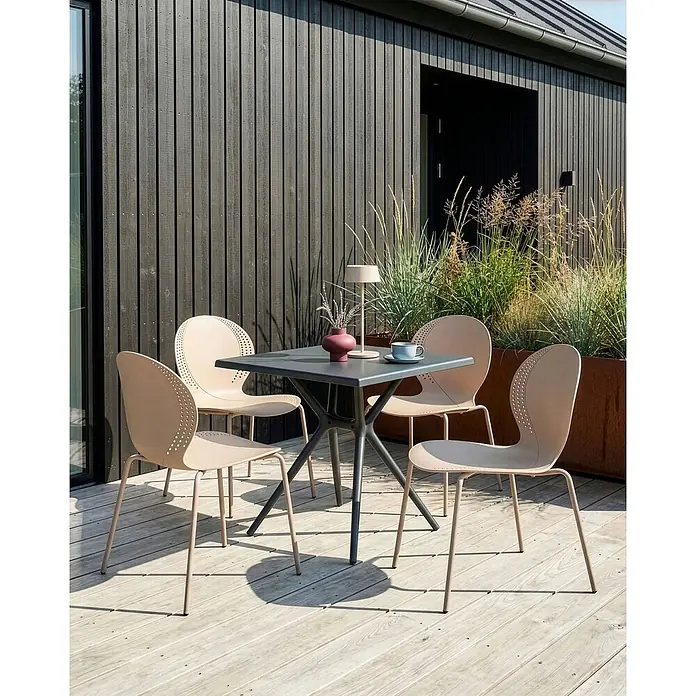4er-Set Esszimmerstuhl MILOS in Beige -  - Beige Outdoorstühle mit perforierten Rückenlehnen und ein quadratischer dunkelgrauer Tisch auf Holzdeck vor modernem Gebäude.